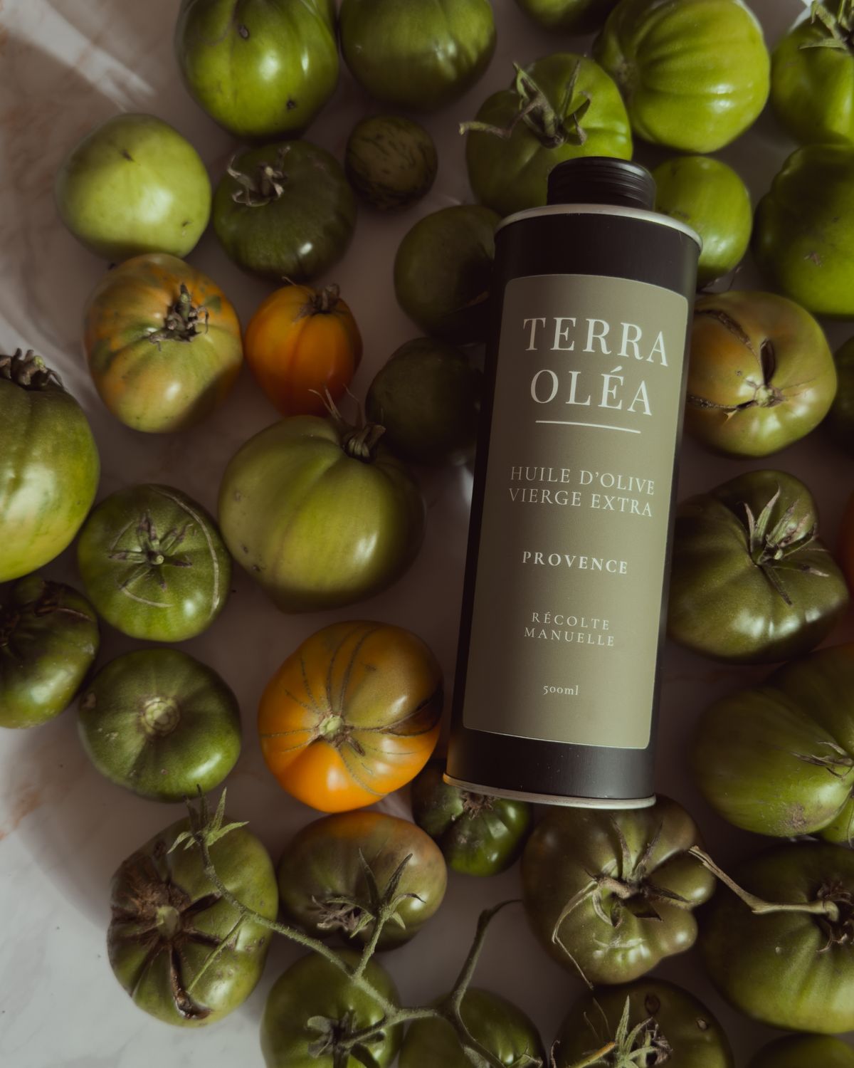 Bidon Terra Oléa posé parmi des tomates vertes et rouges
